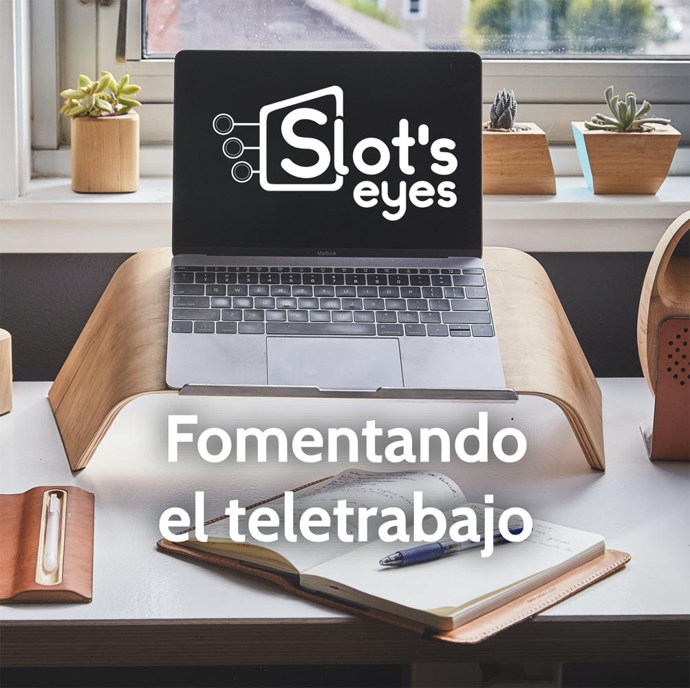 Portátil sobre un soporte junto a una ventana, con el logotipo de Slot's Eyes en pantalla y una libreta abierta al lado