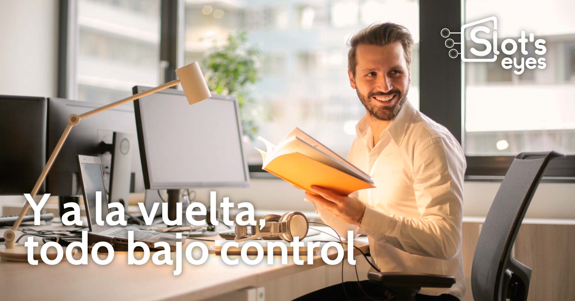 Hombre sonriente en su puesto de oficina, con dos monitores y una carpeta abierta en las manos